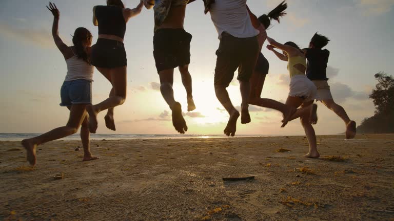 SLOW MOTION - Group of friends running on the beach at sunset with happy emotion. People with party celebration concept. Back Rear View.