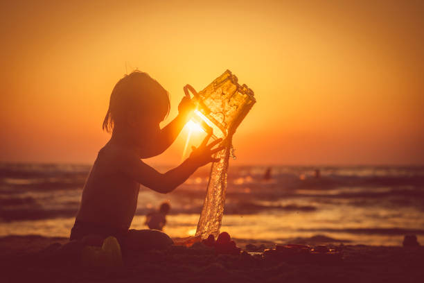 Silhouette of a teenager boy playing to throw water into the air on a beach at sunset in summer in Sicily, Italy