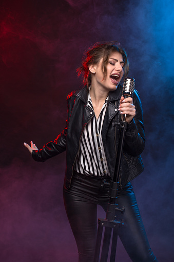 Portrait of expressive rock singer wearing leather jacket and keeping retro style microphone. On smoky dark scene.
