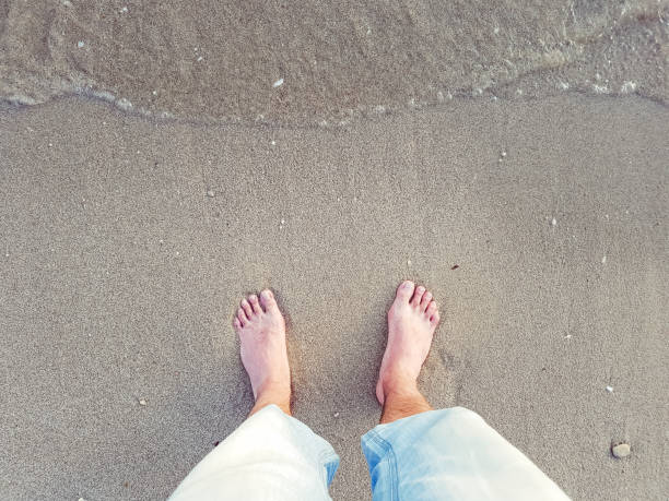 Personal point of view on mans bare foot on sandy beach.