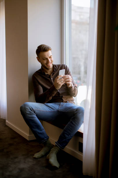 istock Young man using mobile phone in the room by window 1136795412