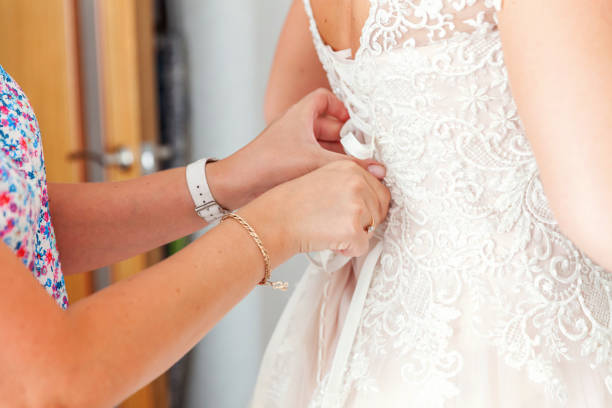 istock Bridesmaid helping bride fasten lacing her wedding white dress before ceremony 1136796529