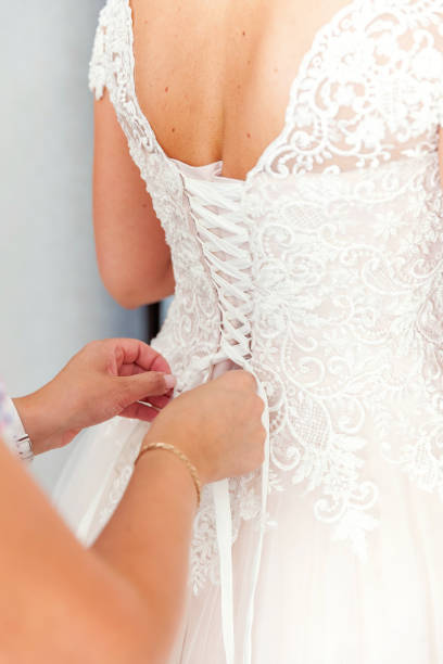 istock Bridesmaid helping bride fasten lacing her wedding white dress before ceremony 1136796609