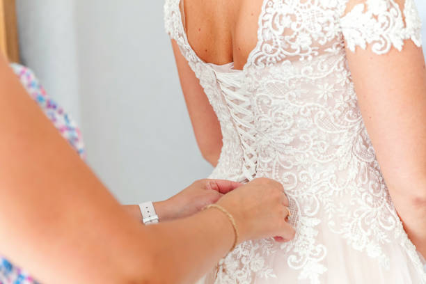 istock Bridesmaid helping bride fasten lacing her wedding white dress before ceremony 1136796655