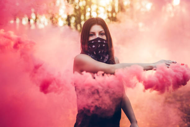 Young caucasian girl with scarf on her face holding smoke fountain in the forest.