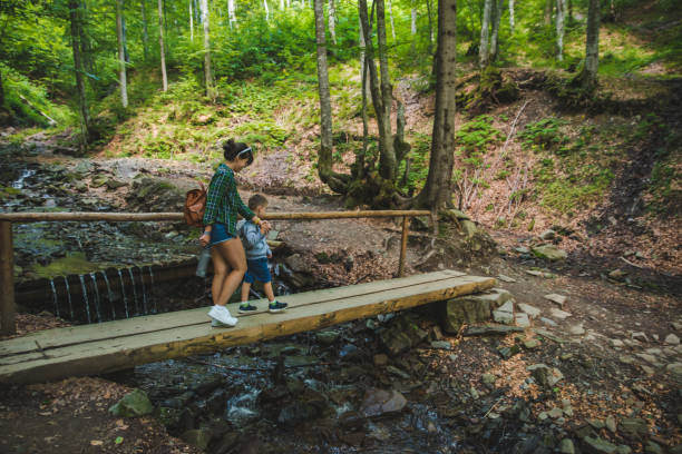 istock mother with kid crossing river via bridge in forest 1136798120