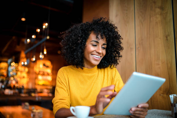 Smiling woman using digital tablet. Beautiful smiling African American woman using digital tablet at the bar. cafe tablet stock pictures, royalty-free photos & images
