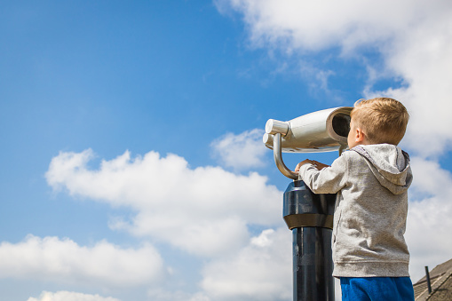 Little boy looking through binoculars and exploring sky at observation view point. Copy space.