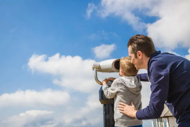 Photo of Little boy and his father through binoculars against the sky.