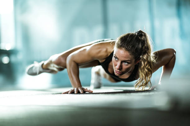 Young female athlete exercising push-ups with in a gym. Athletic woman exercising push-ups in a health club. Copy space. athleticism photos stock pictures, royalty-free photos & images