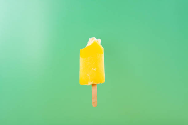 istock yellow popsicle with some bites on a light green background 1136804997