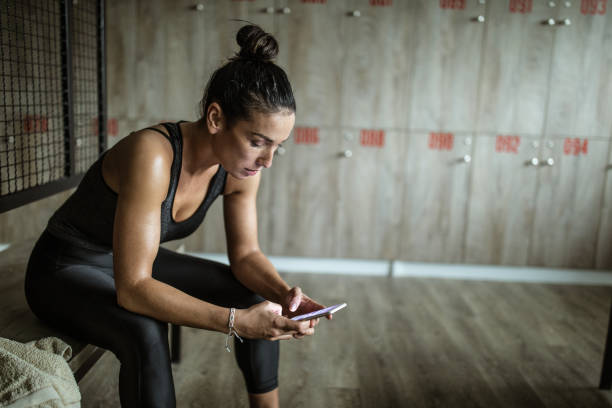 istock Sweaty athletic woman using cell phone in locker room. 1136805801