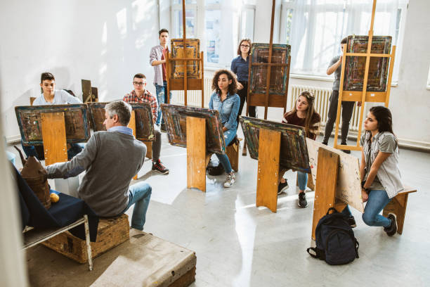 Large group of students having an art class with their teacher in a studio. Male teacher teaching large group of art students on a class at art studio. art class photos stock pictures, royalty-free photos & images