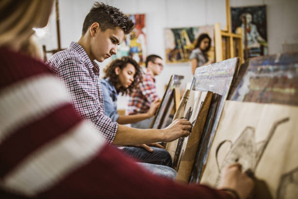 Group of art students drawing paintings at art studio. Group of students drawing their paintings on a class at art studio. Focus is on male student. artistic product stock pictures, royalty-free photos & images