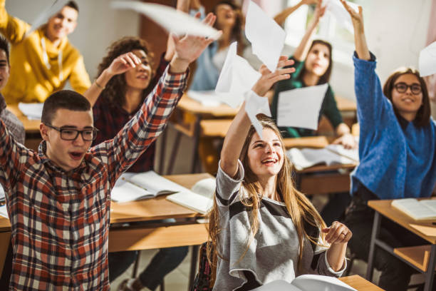 istock Happy students throwing papers while celebrating the end of a school year in the classroom. 1136807426