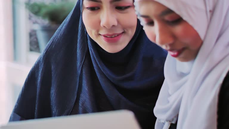 Happy two muslim women shopping online.Young muslim woman in head scarf using laptop in cafe with friends.Arab Youth