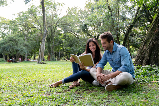 Loving Brazilian couple relaxing at the park reading a book and looking very happy - lifestyle concepts