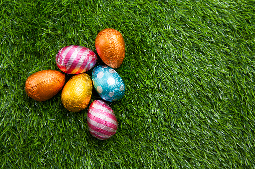 Six coloured foil-wrapped chocolate Easter eggs on an artificial grass surface photographed from above with copy space