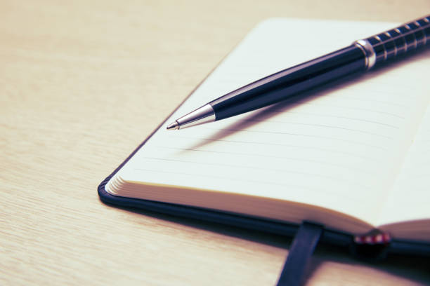istock Black pen lies on the opened note cover on the spring on a light wooden table. 1136825343