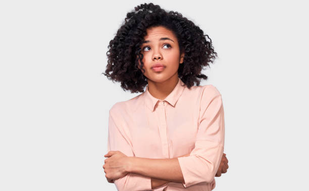 Thoughtful African American woman has thinking expression, looking up away to the blank copy space. Doubtful dark skinned female can`t make choice, has questioned expression, isolated on white. stock photo
