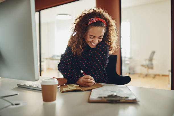 istock Laughing businesswoman writing down notes while working at her desk 1136831201