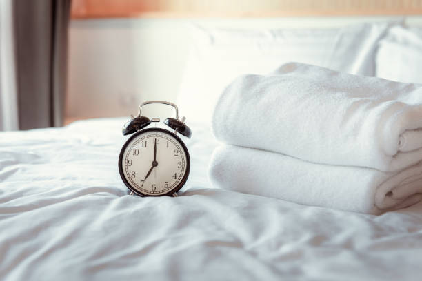 現代の家の寝室のアナログ目覚まし時計、白いカバーベッドの午前7.00 でレトロなタイマー
