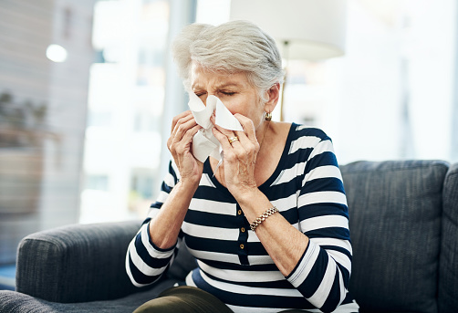 Shot of a senior woman blowing her nose with a tissue at home