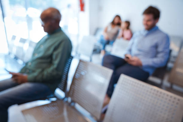 Defocused image of patients waiting at hospital. Multi-ethnic people are at waiting room. They are sitting on seat.