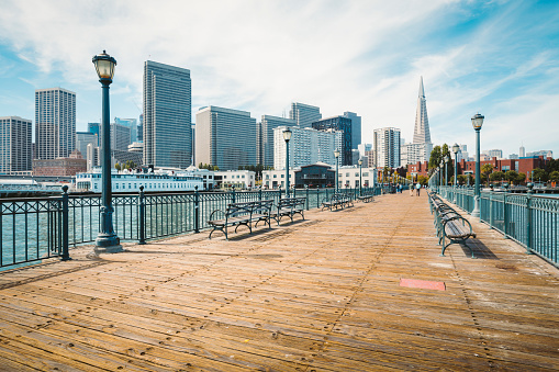 Classic view of historic Pier 7 with the modern financial district of San Francisco on a beautiful sunny day with blue sky and clouds in summer, California, USA