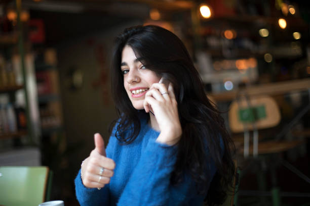 istock Happy confident beautiful woman gesturing thumbs up looking at camera sitting in a cafe while calling by phone 1136843400