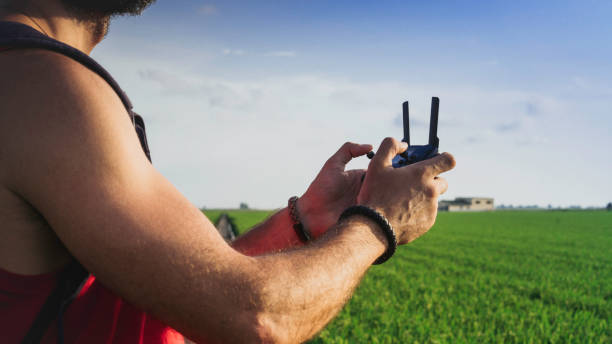 istock Bearded male model use drone remote control to fly device in air.Quadro copter drone flying over sunset green rice fields. Wide banner long format. 1136844811