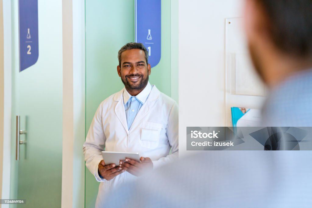 Smiling male doctor looking at patient in corridor Smiling male doctor looking at patient in corridor. Healthcare worker is standing with digital tablet. They are at hospital. 30-34 Years Stock Photo