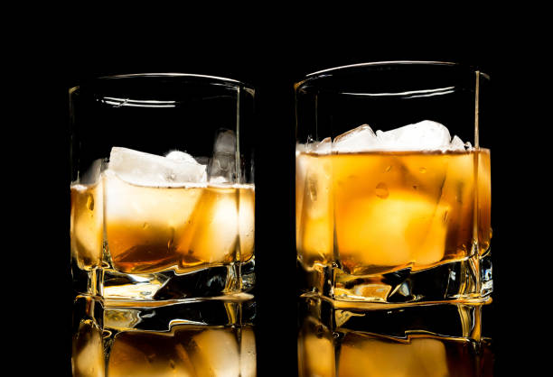 istock Whiskey with ice close up on a glass table isolated on a black background 1136854460