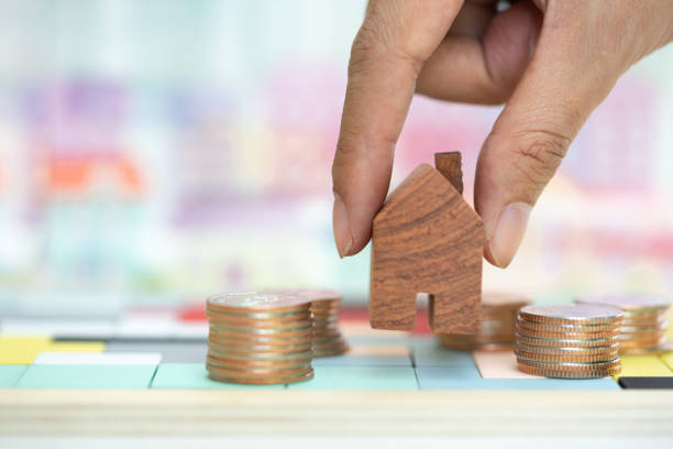 istock Woman's hand putting house model on coins stack. Concept for property ladder, mortgage and real estate investment . 1136857091