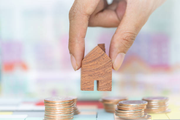 istock Woman's hand putting house model on coins stack. Concept for property ladder, mortgage and real estate investment . 1136857099
