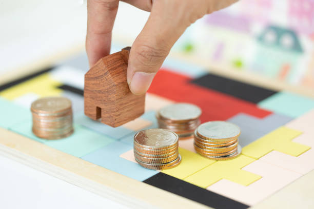 istock Woman's hand putting house model on coins stack. Concept for property ladder, mortgage and real estate investment . 1136857159