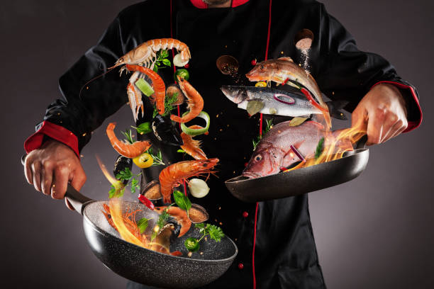 primo piano dello chef che lancia frutta e pesce di mare - dark cooking food food and drink foto e immagini stock