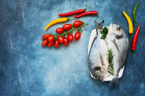 istock Raw sea bream fish with vegetables on blue background. Top view, copy space. 1136858097
