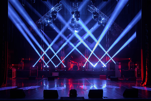Rear view of large group of people enjoying a concert performance. There are many hands applauding and taping the show. Multi colored lasers and spot lights firing from the stage.\nSilhouettes have been significantly liquified.