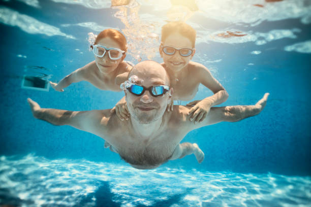 padre e figli che giocano sott'acqua nella piscina del resort - cheerful swimming pool happiness resort swimming pool foto e immagini stock