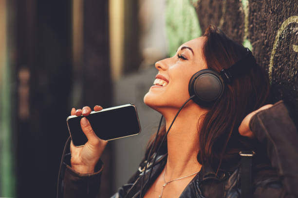 若い女性は路上でヘッドフォンを介して音楽を楽しむ - young adult technology beautiful singing ストックフォトと画像