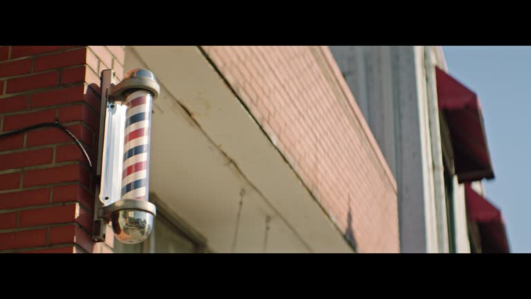 Traditional red, white, and blue striped barber shop pole turns on outside of small town brick and mortar barber shop.