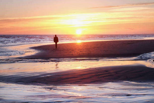 istock A solitary man walking across a deserted sandy beach at sunset 1136878476