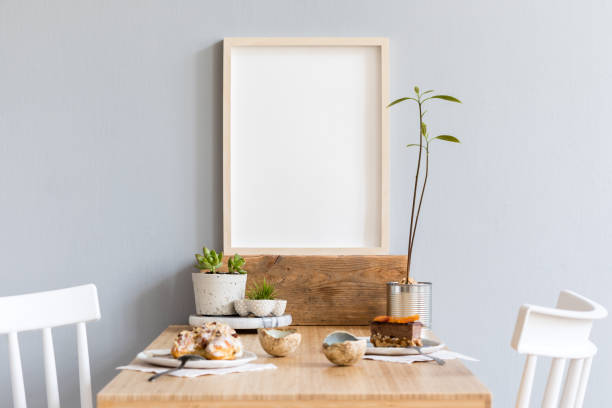 istock Stylish and modern interior design of kitchen space with small wooden table with mock up photo frame, avocado plant, succulents, cups of tea and tasty dessert. Scandinavian space decor. 1136892183