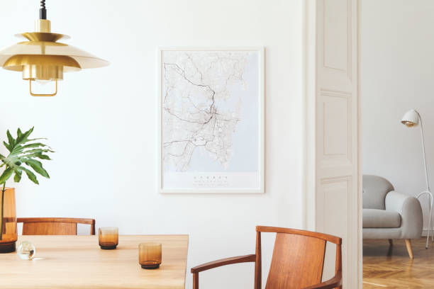 istock Stylish and eclectic dining room interior with mock up poster map, sharing table design chairs, gold pedant lamp and elegant sofa in second space. White walls, wooden parquet. Tropical leafs in vase. 1136894731