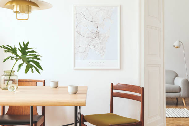 Stylish and eclectic dining room interior with mock up poster map, sharing table design chairs, gold pedant lamp and elegant sofa in second space. White walls, wooden parquet. Tropical leafs in vase. Stylish and modern dining room interior with mock up poster. Eclectic decor. wooden bleachers stock pictures, royalty-free photos & images