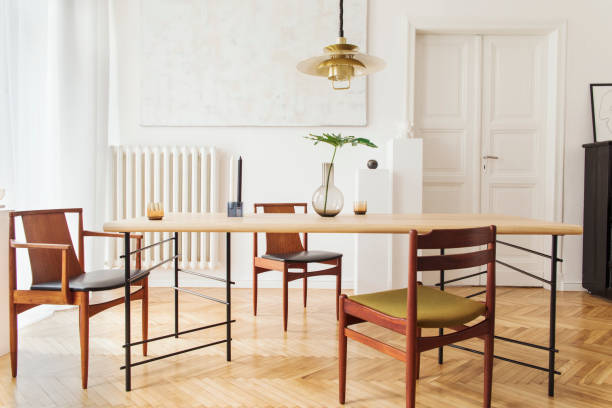 istock Eclectic and elegant dining room interior with design sharing table, chairs, gold pedant lamp, abstract paintings, piano and stylish accessories. Eclectic decor. Brown wooden parquet. Real photo. 1136896439