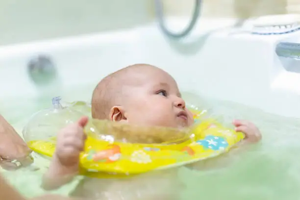 Photo of Cute little infant boy swimming with inflatable neck swim ring in bath. Baby having fun during water hygienic activities. Child healthcare and development concept