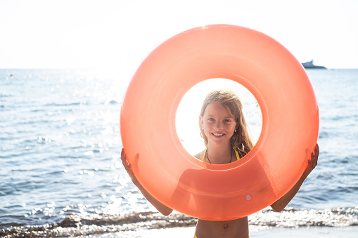 A beautiful girl goes swimming in the sea with floating ring and looking through it