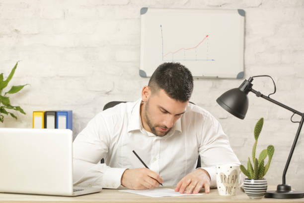 istock A handsome young businessman sitting at his desk in front of the laptop, signing a document. Just an ordinary day at the office 1136912607